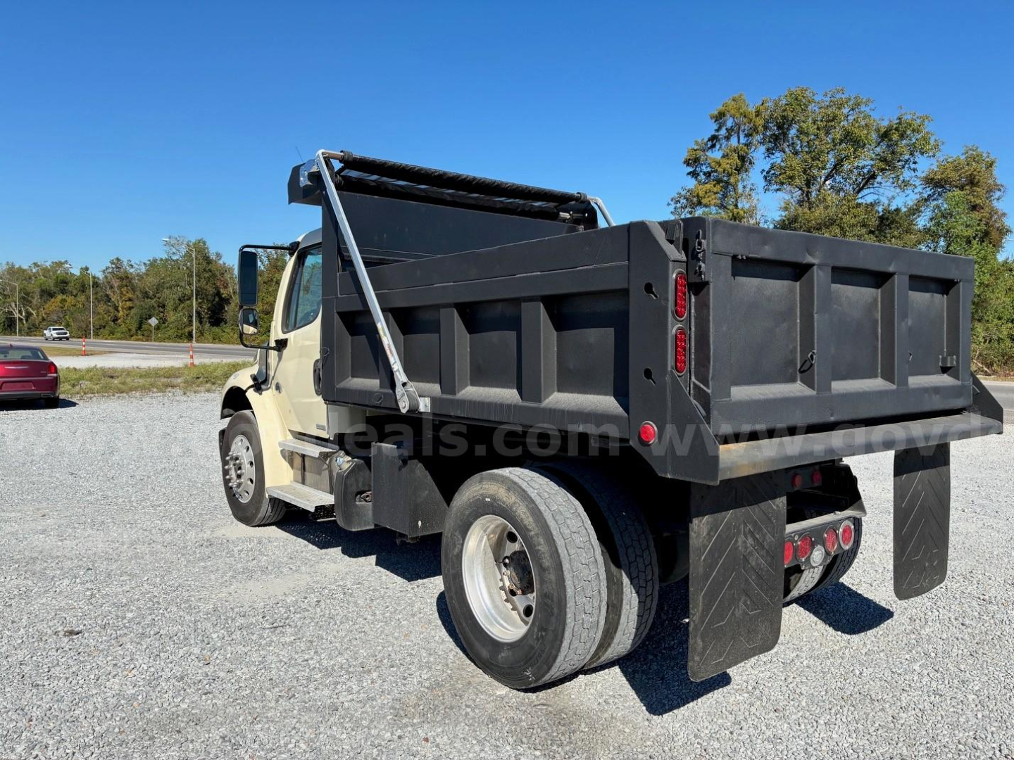 Dump truck bed of a Freightliner M2 106 dump truck showing rear and side view, black dump body, dual rear wheels, hydraulic hoist, white cab.