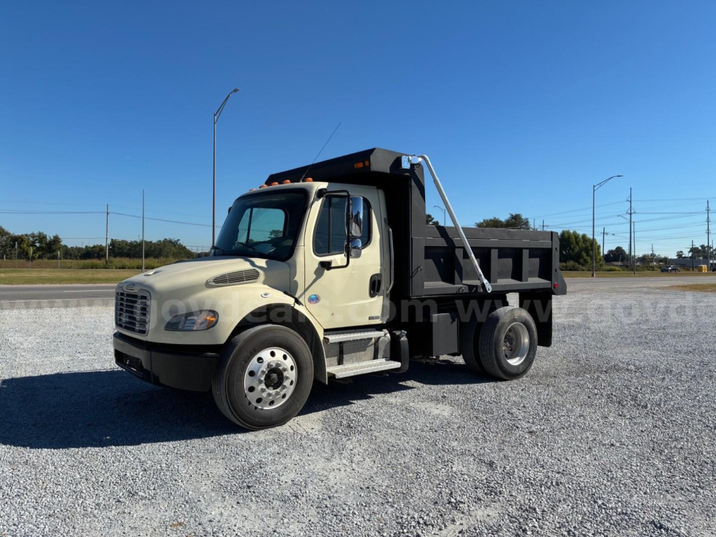 2009 Freightliner M2 106 dump truck in serviceable condition with beige cab and black dump bed, side view, open gravel lot.