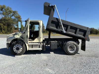 Freightliner M2 106 dump truck side view showing dump bed raised and hydraulic cylinder visible.