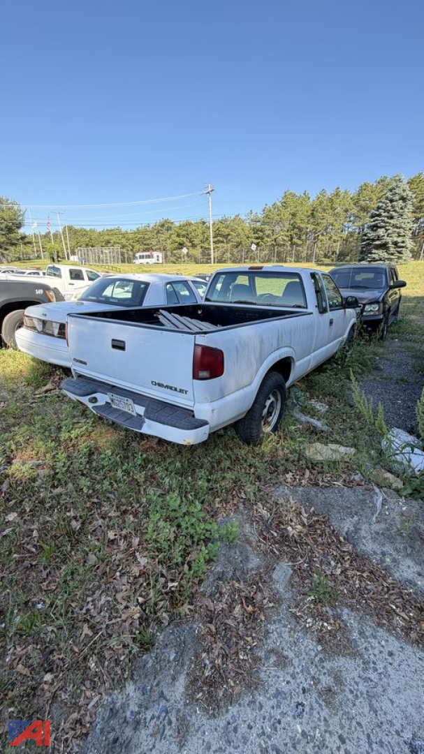 Rear view of a white 1998 Chevrolet S-10 pickup truck with the bed open, showing tailgate and bumper; other trucks in background.