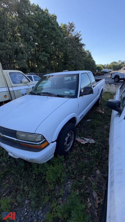 Front-left view of a white 1998 Chevrolet S-10 pickup truck in a grassy lot, with other vehicles nearby.