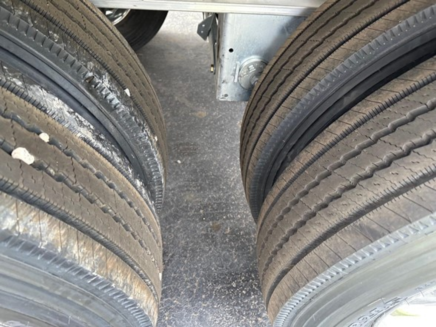 Trailer tires and suspension components visible between two axles, showing dual rear wheels with tread and rim details.