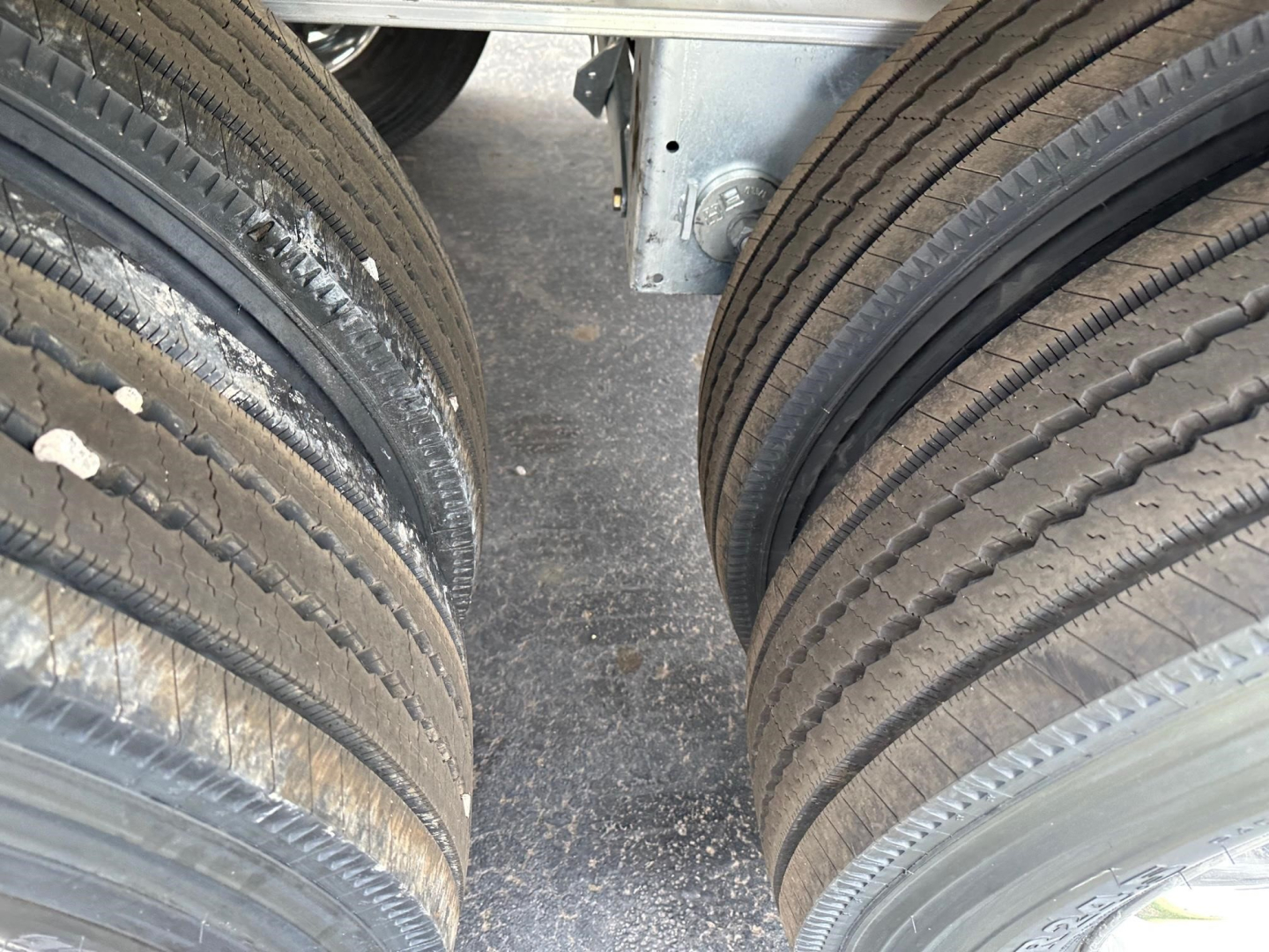 Trailer tires sidelined showing dual axles and frame; close-up of tandem wheel assembly with treaded tires and metallic undercarriage.