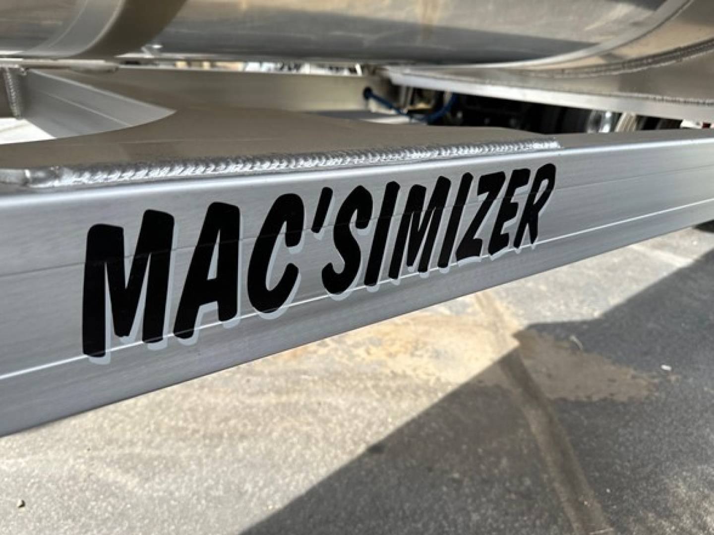 MAC'SIMIZER trailer component showing MAC'SIMIZER branding on aluminum edge with weld seam and fender in background.