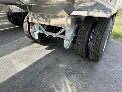 Dump trailer axle area with dual rear axles and metallic frame, showing wheels and suspension components.
