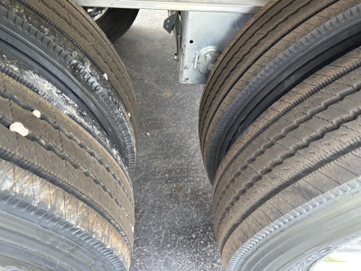 Trailer tires sidelined showing dual axles and frame; close-up of tandem wheel assembly with treaded tires and metallic undercarriage.