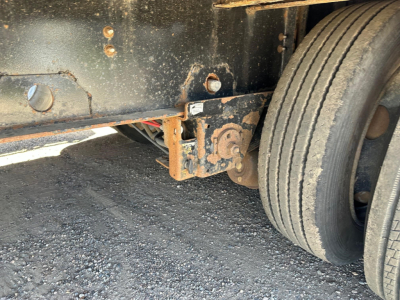 Trailer frame with dual axle, rear undercarriage showing landing gear and hydraulic components, close-up of suspension area and wheel with visible rusted hub and metal brackets.