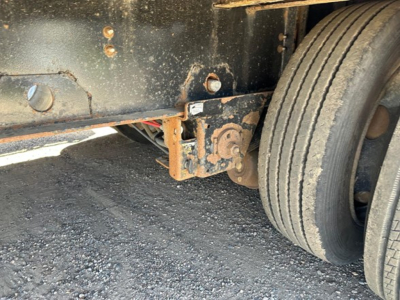 Trailer undercarriage showing rear axle, dual wheels, and suspension mounting with wear indications and riveted frame.