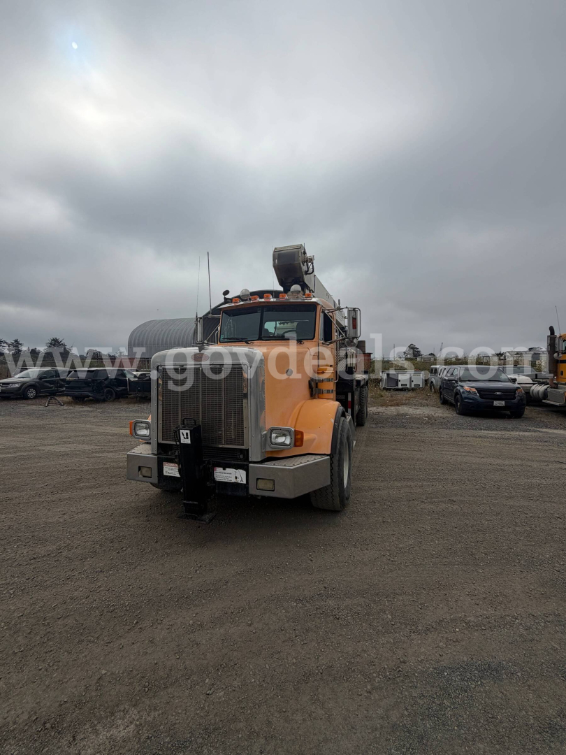 Peterbilt 357 truck in a dirt lot, orange cab, front view with chrome grille and bumper, visor lights, and sleeper cab.