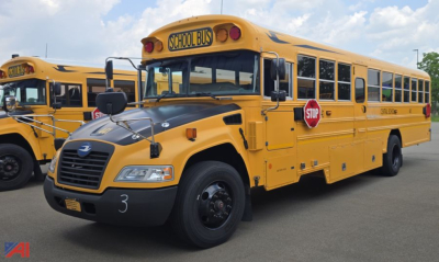 School bus with yellow exterior and STOP sign extended, front view showing hood and headlights, blue Bird Vision branding on bus