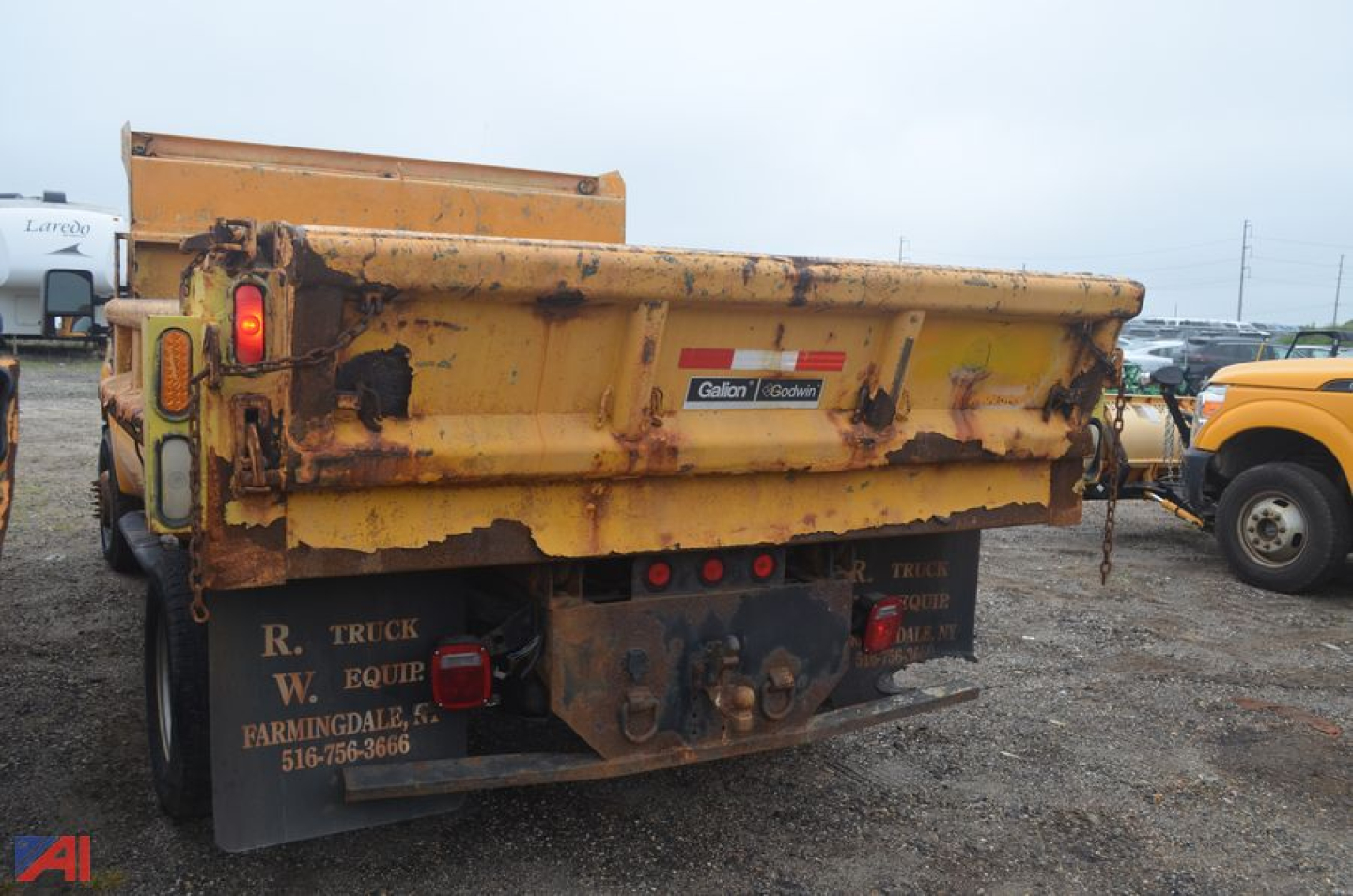 Dump truck bed of a 2010 Ford F-350 Super Duty dump truck showing yellow bed with rusted areas and rear bumper with lights and chain hangs.