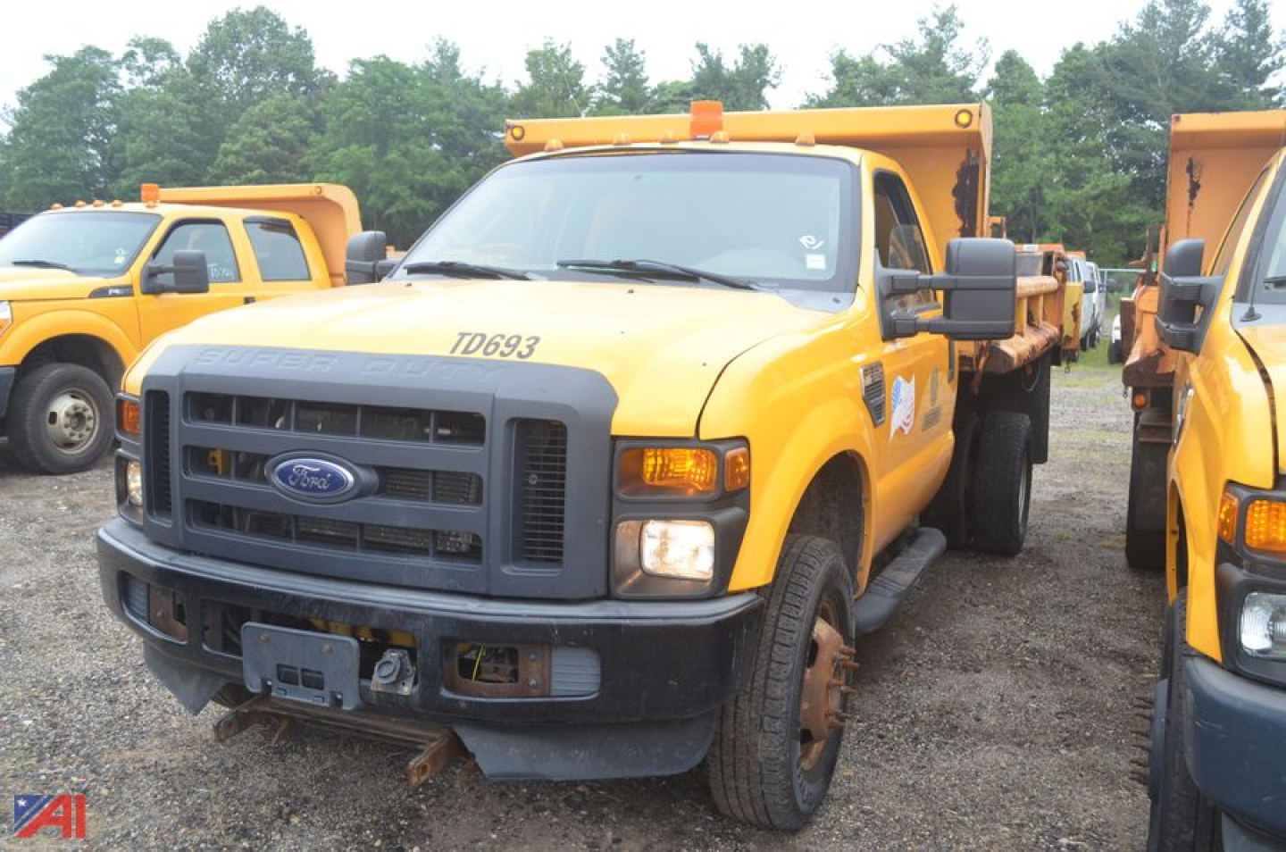 Ford F-350 Super Duty dump truck in yellow with black grille, front view, VIN/ID number on hood, in a lot with other yellow trucks.