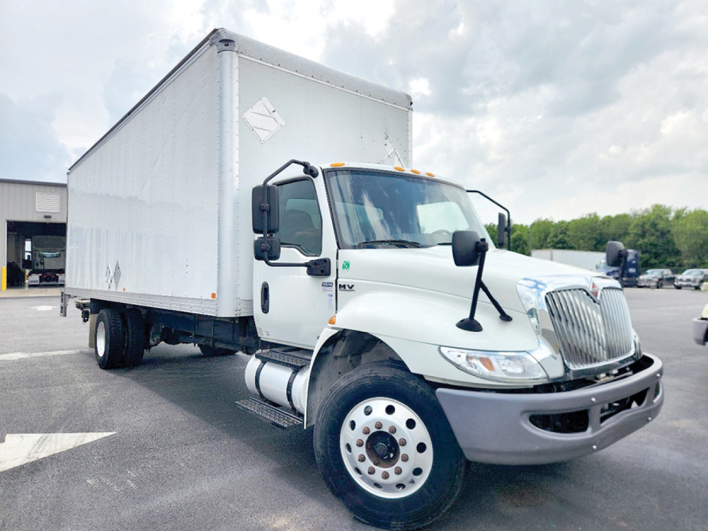 Truck engine bay and cab of a white 2021 International 4300 conventional daycab front-left view.
