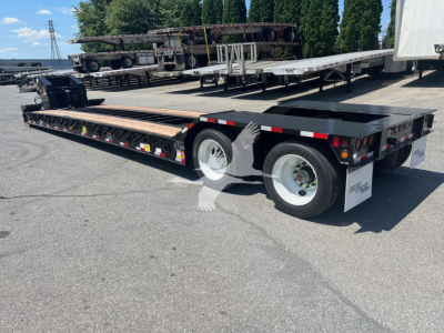Trailer: lowboy trailer with dual rear axles and long flatbed, black with white wheels, side reflectors, and rear underride protection; shows VL088762 stock tag and VIN plate.