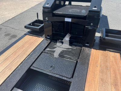 Trailer deck with metal steps and storage hatches, black frame, wooden deck sections, diamond plate access covers, and components for a lowboy trailer.