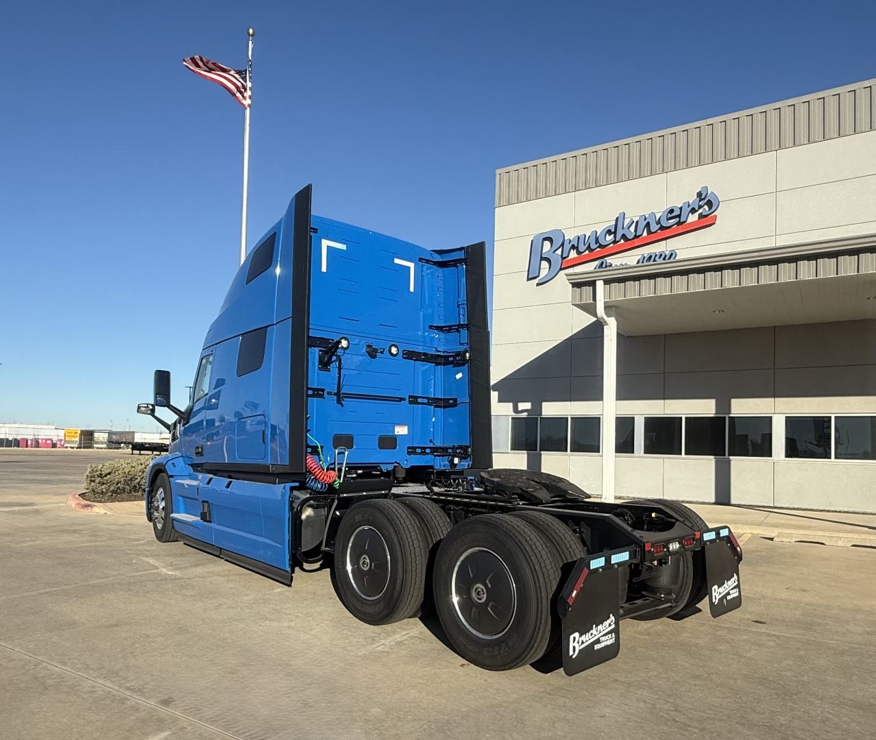 Truck cab and chassis of a blue Mack PR64T76H in a dealership lot showing rear wheels and trailer connections.