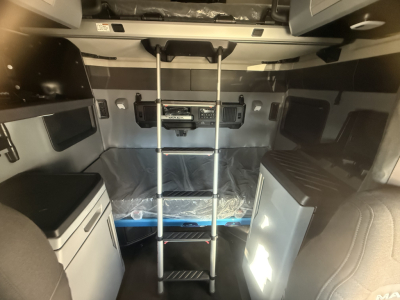 Cab interior of a new 2026 Mack PR64T76H sleeper truck showing ladder, bunk bed, cabinets, and control panel area with storage cabinets on both sides.