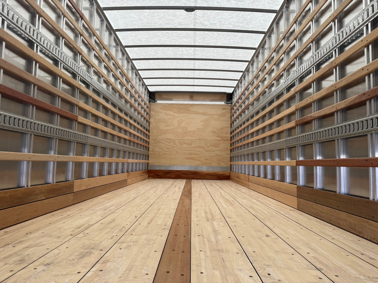 Isuzu FTR truck cargo box interior showing wooden floor and metal side rails with tiedown rails and van-like ceiling. URL not shown.