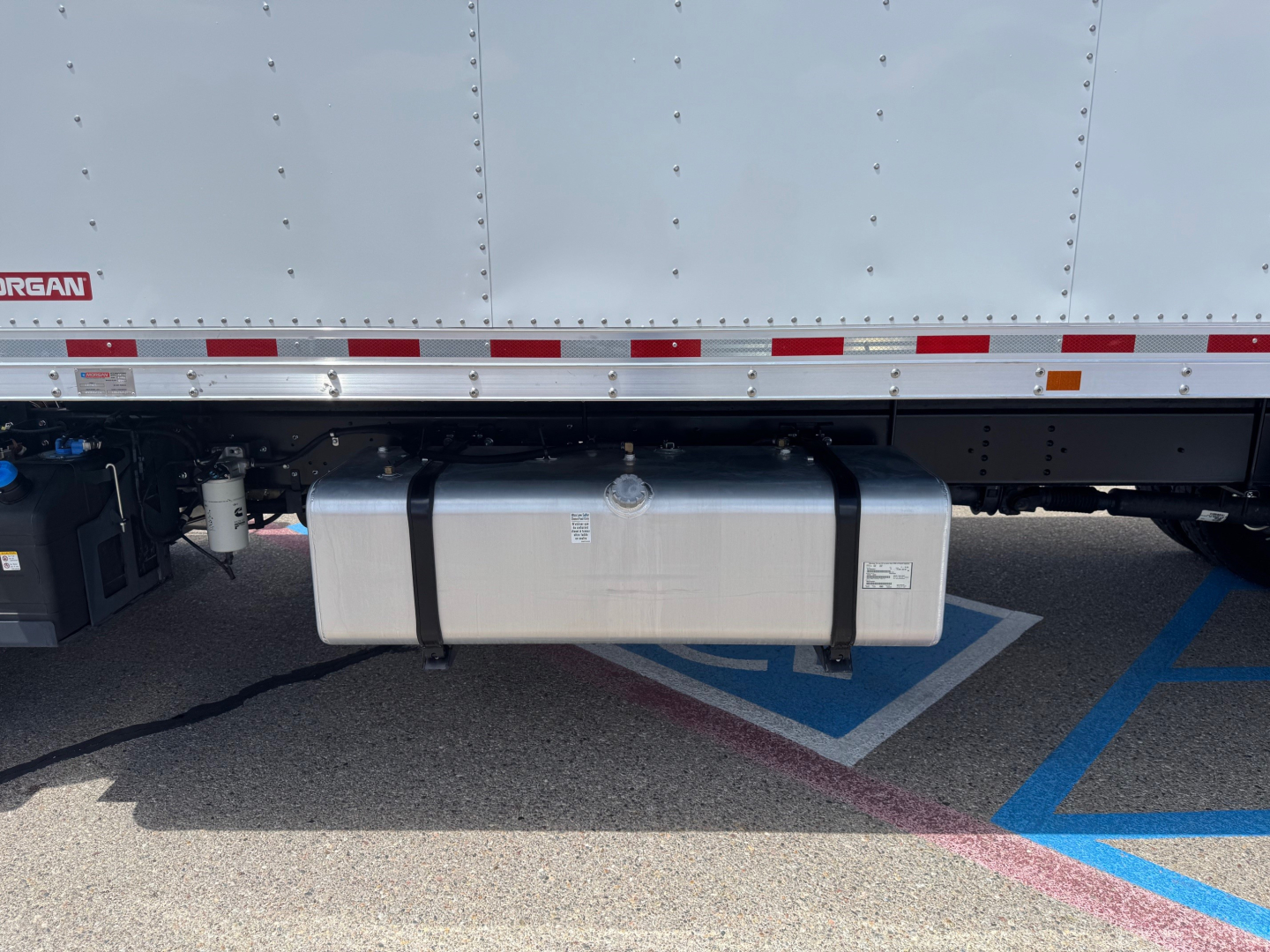Isuzu FTR truck undercarriage showing silver rectangular diesel fuel tank with black straps and side bands.