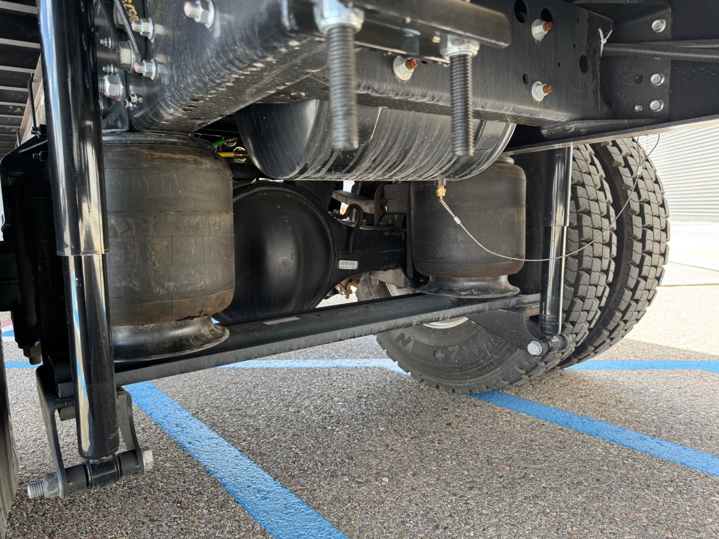 Isuzu FTR undercarriage showing suspension, air tanks, frame, and dual tires in a service lot.