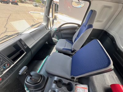 Isuzu FTR cab interior showing driver seat and passenger seat with blue fabric, dashboard controls, gear shifter, and cup holders.