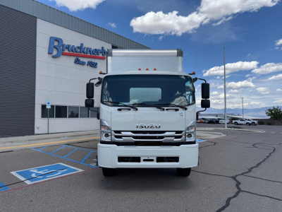 Isuzu FTR box truck front view in dealership lot with Bruckner's building in background and clear blue sky.