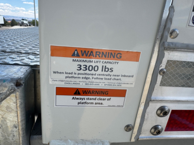 Isuzu FTR side panel showing warning labels: 'MAXIMUM LIFT CAPACITY 3300 lbs' with additional instruction text, and 'Always stand clear of platform area' warnings.
