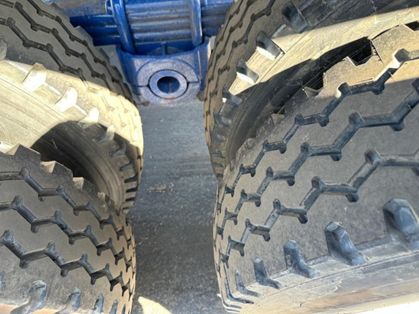Two big off-road trailer tires with tread and blue frame visible between, wheel hubs in center.