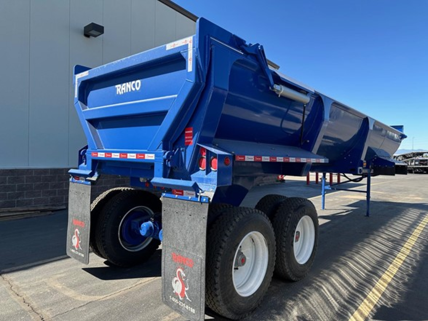 Blue Ranco ED26-34 dump trailer viewed from rear-left side showing dual rear wheels and hydraulic tailgate with white RANCO text.