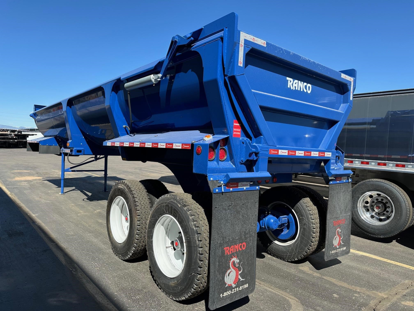 Ranco ED26-34 dump trailer in blue, side view showing dual rear axles with large tires, rear bumper and tailgate with RANCO branding.