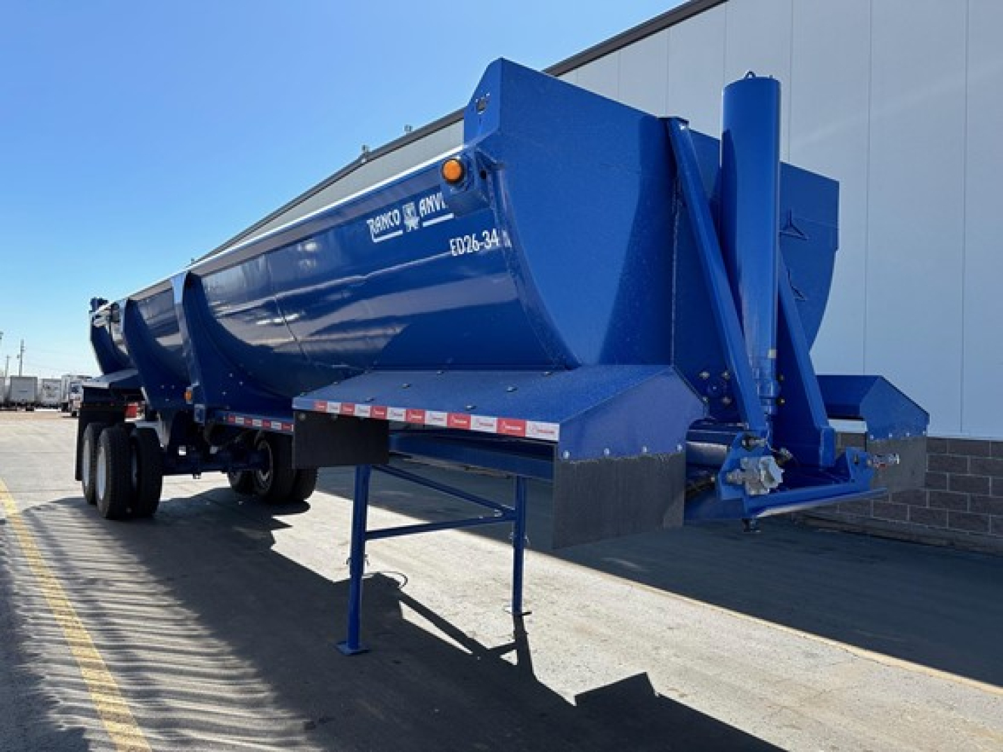 Dump trailer showing blue Ranco Ed26-34 with stock number NE10702 and VIN 150108813642, side-mounted storage, rear hitch, and landing gear.