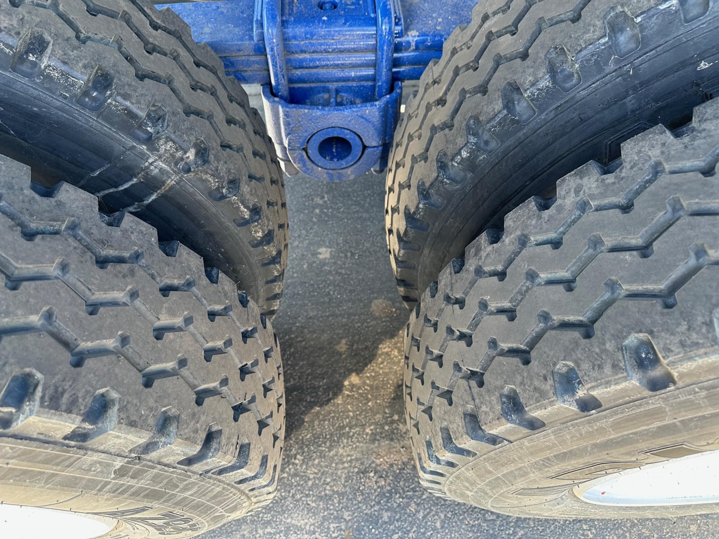Dual rear tractor-trailer tires with large treads on a blue axle, showing the gap between the tires and a central blue frame.