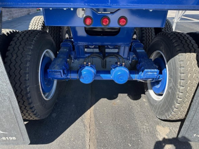 Rear view of a blue heavy-duty trailer axle assembly showing dual tires, suspension, and blue hubs.