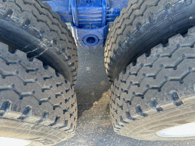 Dual rear tractor-trailer tires with large treads on a blue axle, showing the gap between the tires and a central blue frame.