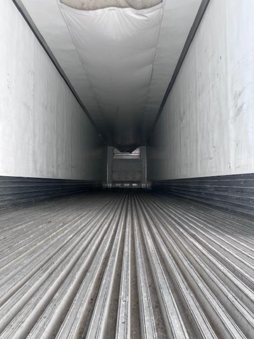 Interior of a trailer cargo space with corrugated floor and white sidewalls. Front landing gear area visible in distance.
