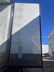 Trailer rear view showing white curtain-sided trailer with CS5208 marking and black lower skirting, under clear blue sky; other trailers visible in background.