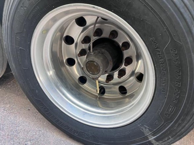 Wheel of a utility trailer showing a radial tire with alloy rim and lug nuts; no visible text besides tire sidewall markings.