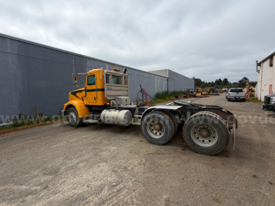 Peterbilt 367 truck tractor in a yard, side view showing yellow cab, long chassis, dual rear axles with large tires, no trailer attached.