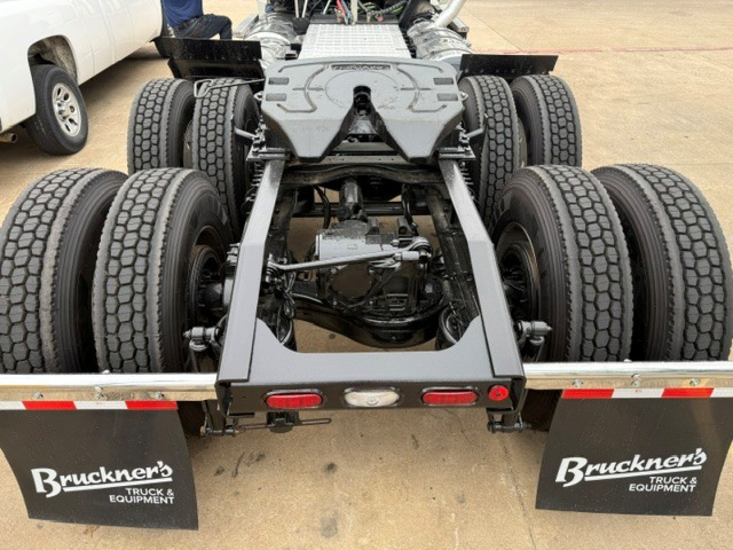 Truck rear chassis of a 2019 Mack PI64T showing dual rear axles and drive line, with mudflaps labeled Bruckner's Truck & Equipment.