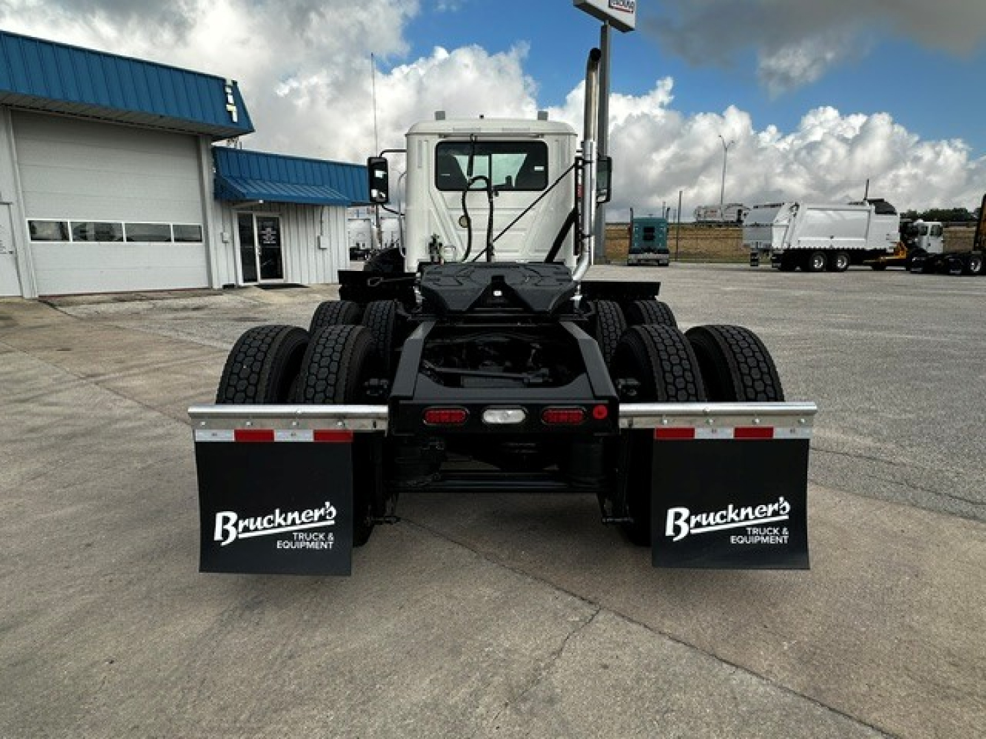 Conventional daycab truck chassis from rear showing dual rear axles, white cab, black mud flaps labeled Bruckner Equipment, and rear reflectors.