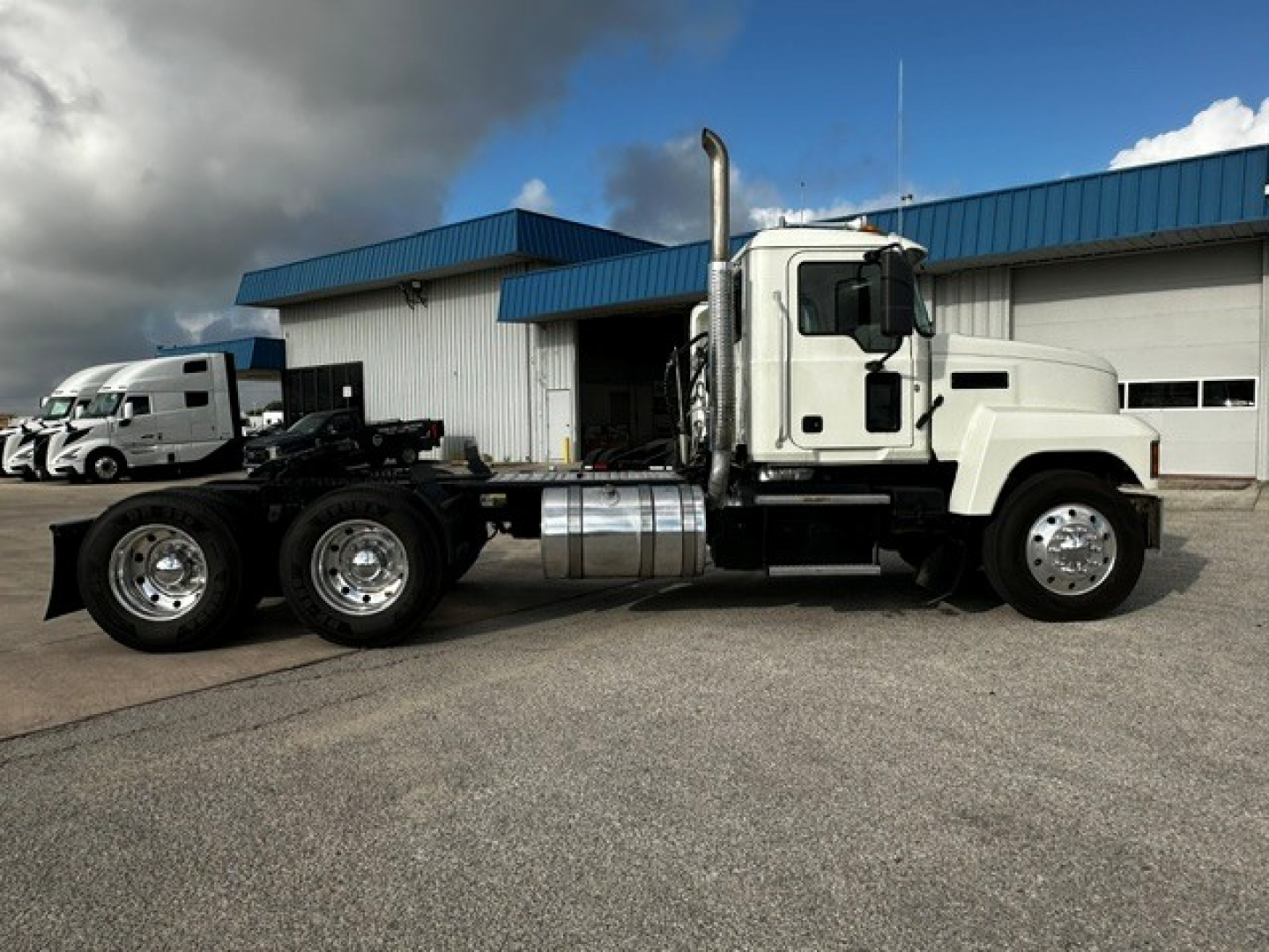 Truck cab and chassis of a white 2019 Mack PI64T conventional daycab showing side view with dual rear axles and chrome fuel tank.