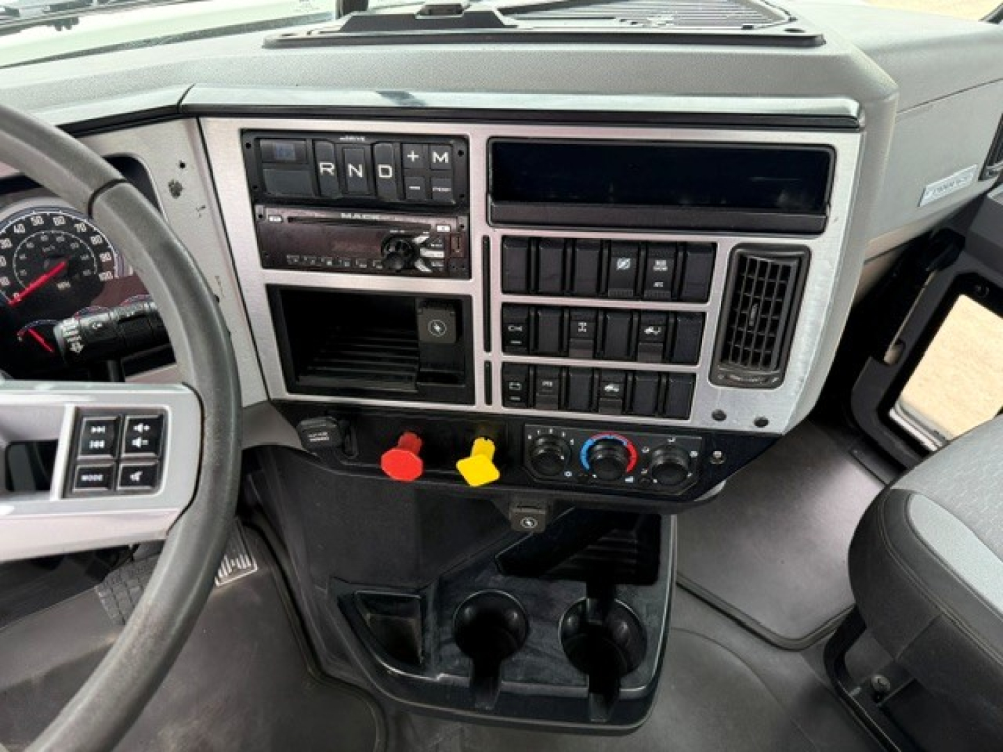 Dashboard of a 2019 Mack PI64T conventional daycab showing steering wheel, gear selector area, auxiliary switches, and control panel with climate controls and storage compartments.