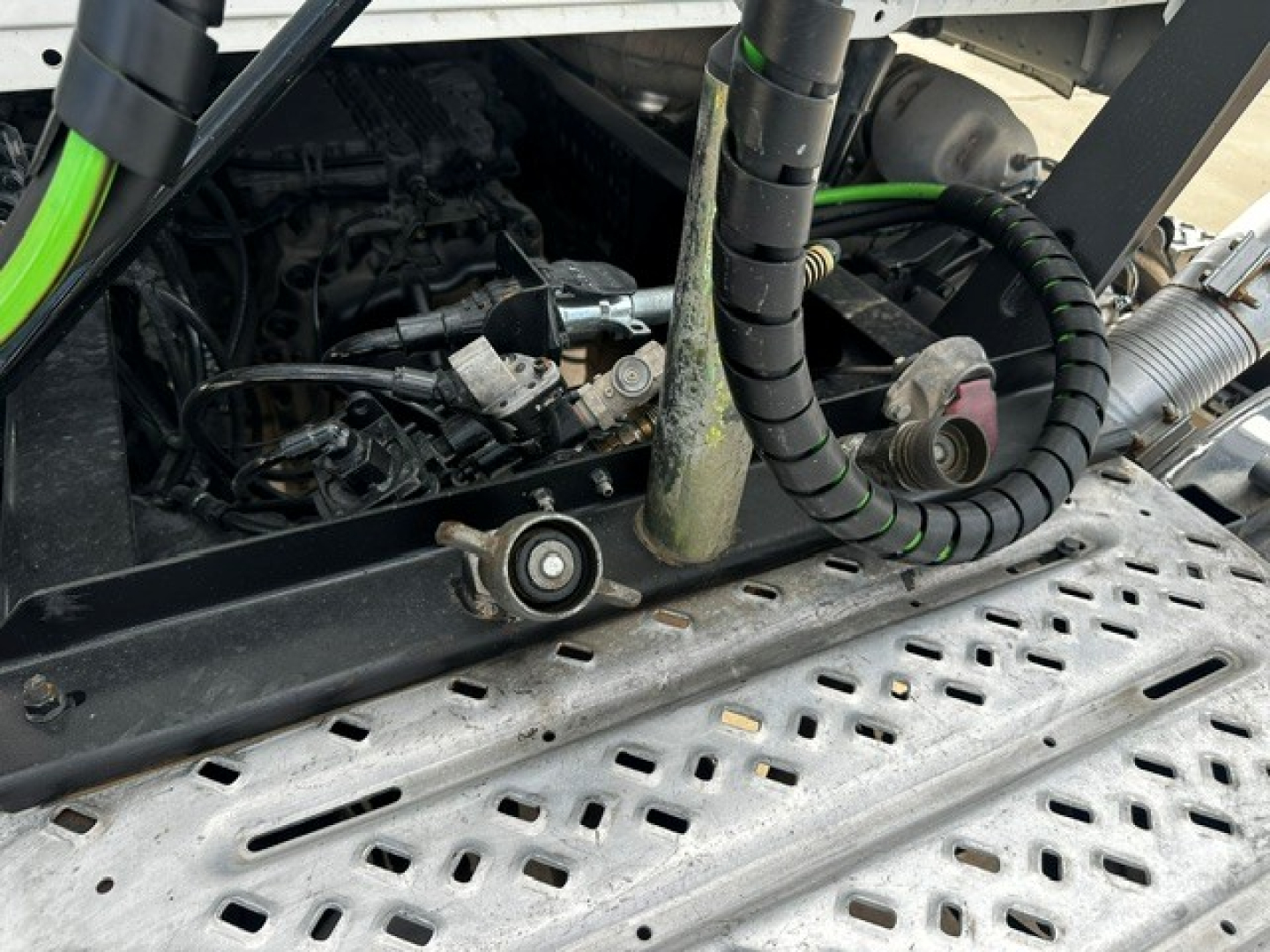Mack PI64T cab area showing engine components and electrical harnesses in view, with metal perforated step and tubing nearby.