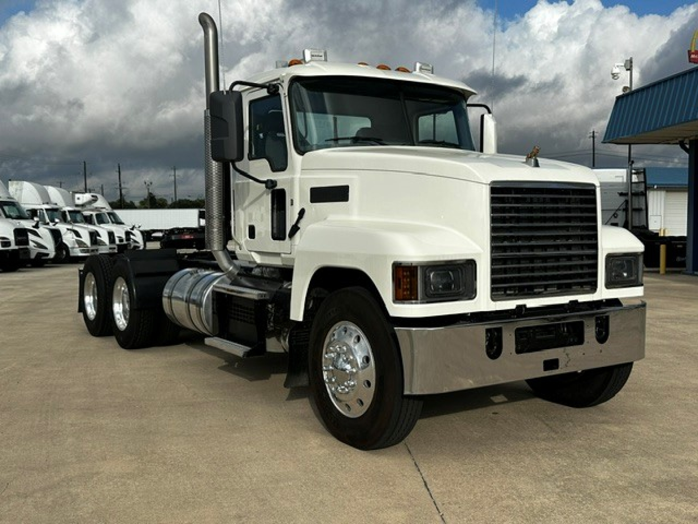 Mack PI64T conventional daycab tractor showing front grille and bumper with dual rear axles and chrome fuel tanks.
