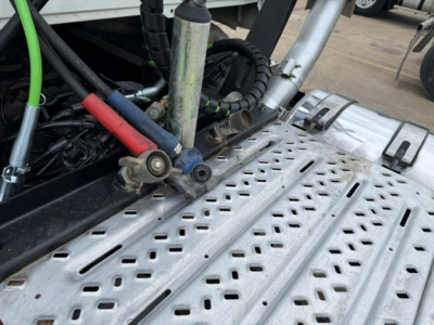 Mack PI64T engine bay area with hydraulic lines and metal steps; close-up showing hoses, fittings, and perforated aluminum side step.