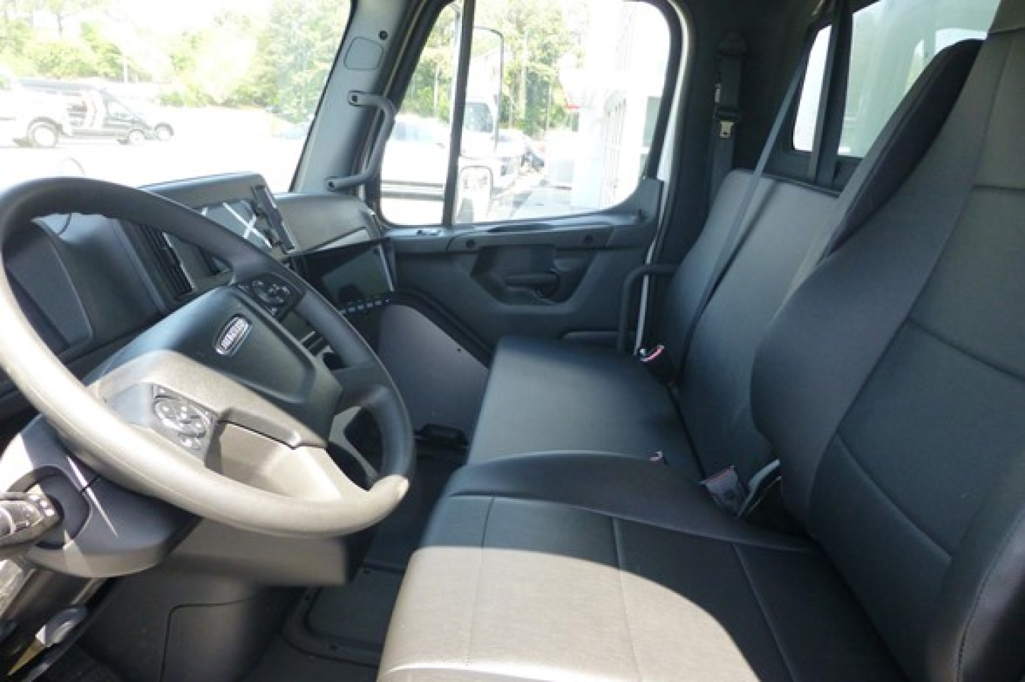 Freightliner M2 106 cab interior showing steering wheel, driver seat, and front passenger seat with center console and dashboard visible.
