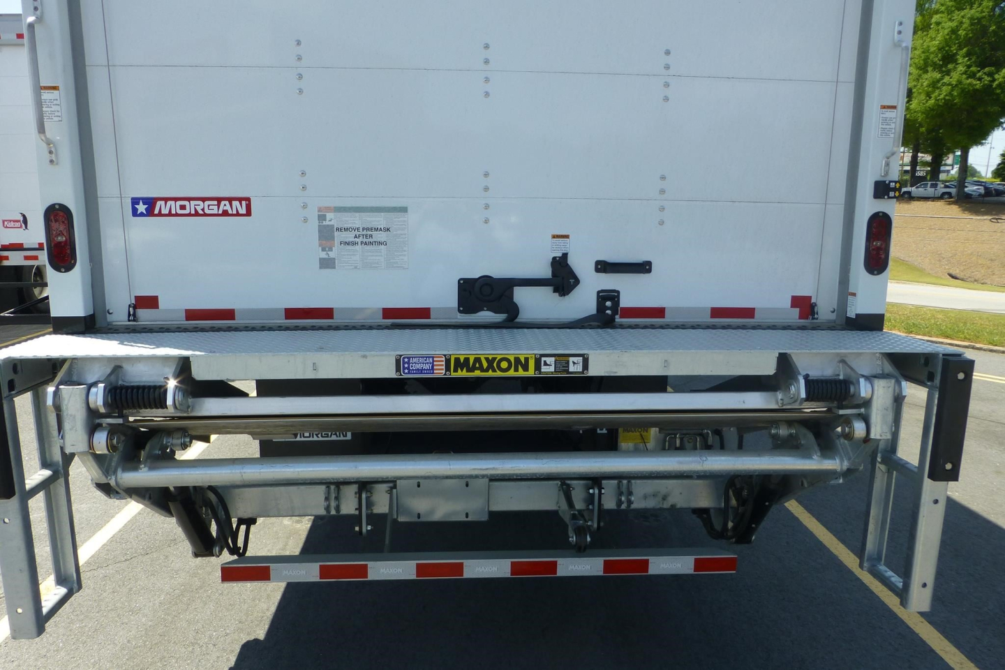 Rear view of a Freightliner M2 106 truck with a Maxon hydraulic tailgate system. Visible text includes MORGAN sticker, MAXON label, and small instruction placards on the tailgate.