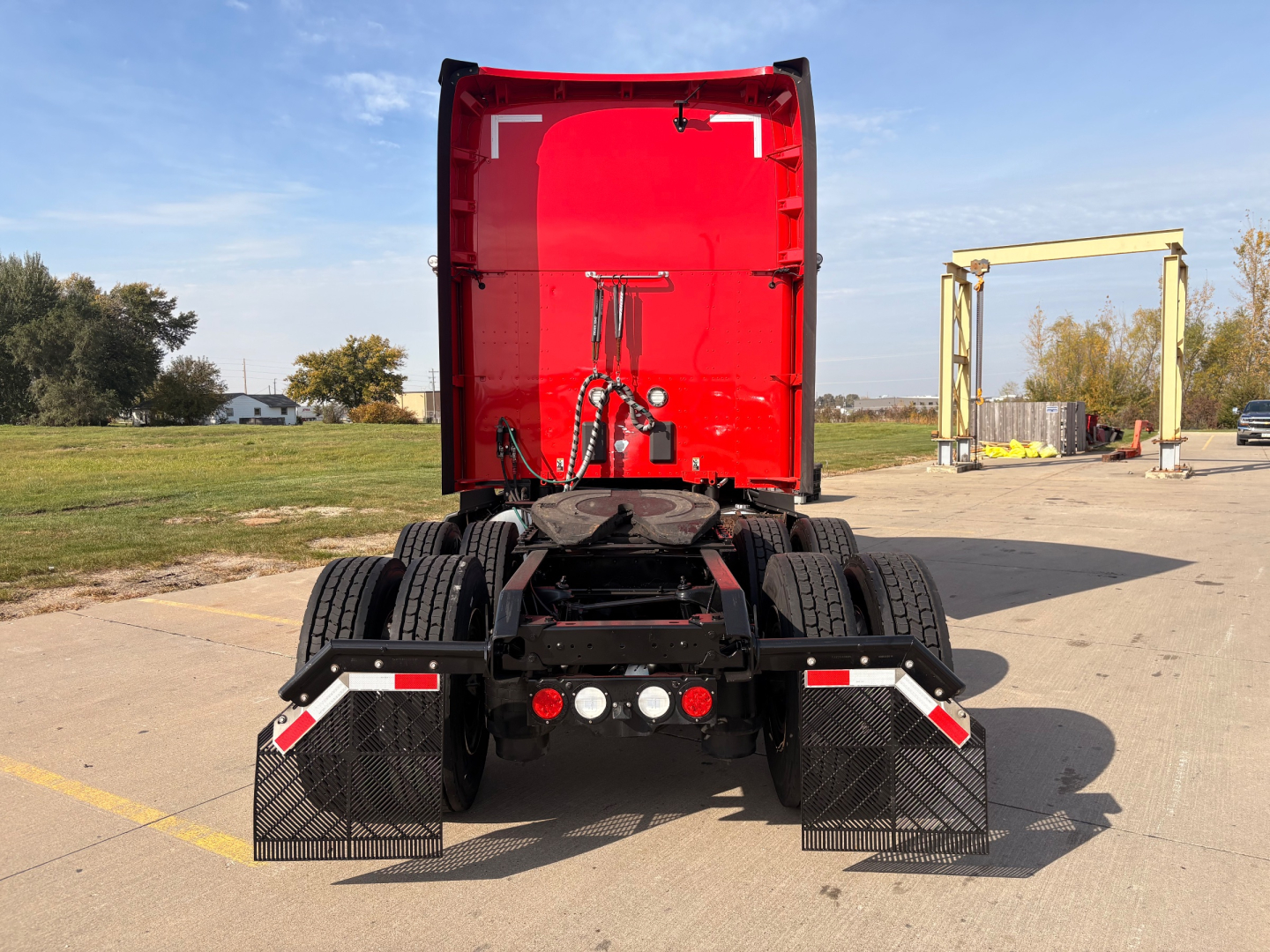 Kenworth T680 truck rear view showing red cab, chassis, dual rear axles, and mudflaps with reflective chevrons.