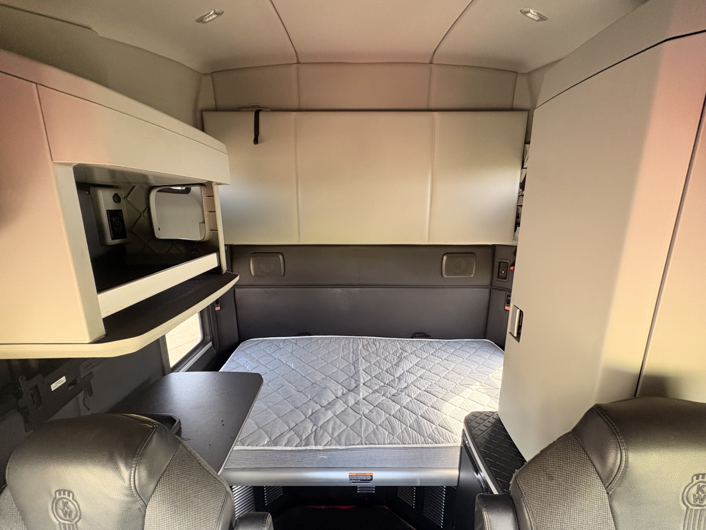 Kenworth T680 sleeper cab interior with mounted storage cabinets and a quilted mattress pad in the sleeping area
