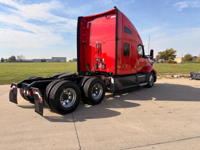 Kenworth T680 tractor in red with sleeper cab, viewed from rear-left side, showing dual rear axles and fifth-wheel attachment.